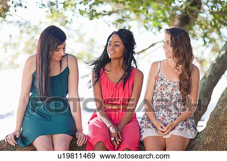 Stock Photo - Smiling women sitting on a tree branch. Fotosearch