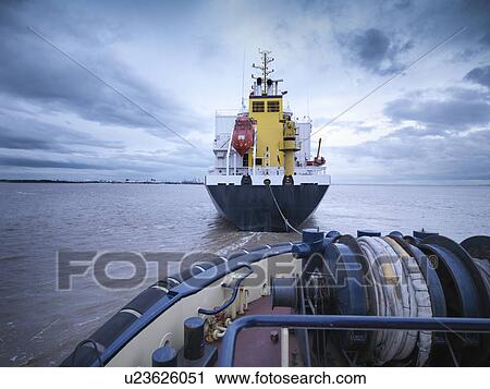 Stock Image - Tugboat towing ship out to sea. Fotosearch