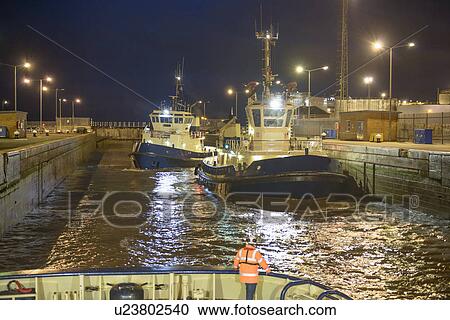 Stock Image - Tugboats docked in harbor at night. Fotosearch
