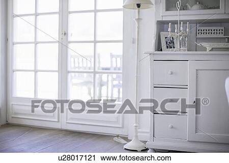 Stock Image - White drawers and lamp by windows. Fotosearch