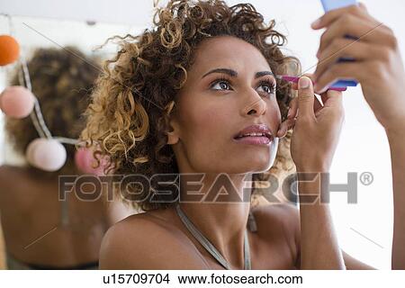 Picture - Woman applying make up in mirror. Fotosearch