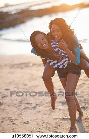 Stock Image - Woman carrying friend on beach. Fotosearch