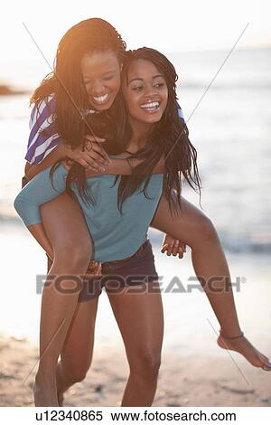Stock Photography - Woman carrying friend on beach. Fotosearch