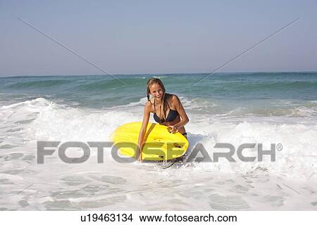 Woman carrying surfboard in waves View Large Photo Image Picture - Woman carrying surfboard in waves. Fotosearch