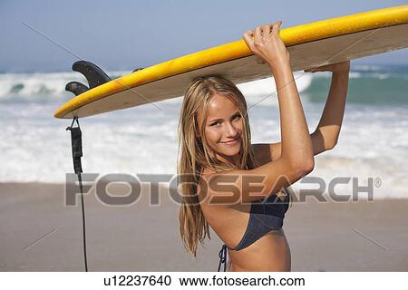 Stock Image - Woman carrying surfboard on beach. Fotosearch