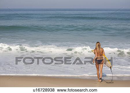 Stock Photo - Woman carrying surfboard on beach. Fotosearch