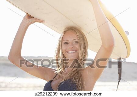 Stock Photo - Woman carrying surfboard on beach. Fotosearch