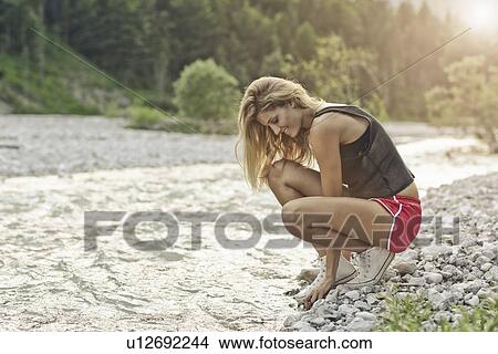 Picture - Woman crouching on gravel river bank. Fotosearch