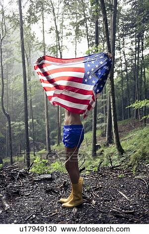 Stock Image - Woman holding American flag in forest. Fotosearch