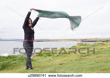Stock Image - Woman playing with scarf in grassy field. Fotosearch