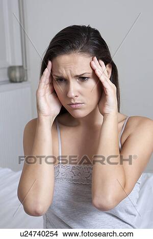 Picture - Woman rubbing her temples on bed. Fotosearch