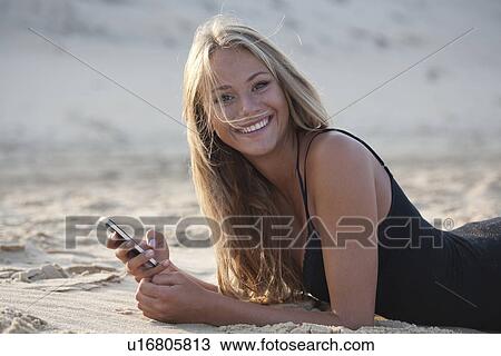 Stock Image - Woman using cell phone on beach. Fotosearch