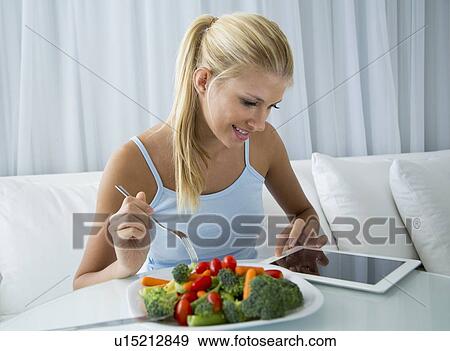 Stock Photo - Woman using tablet computer and eating. Fotosearch