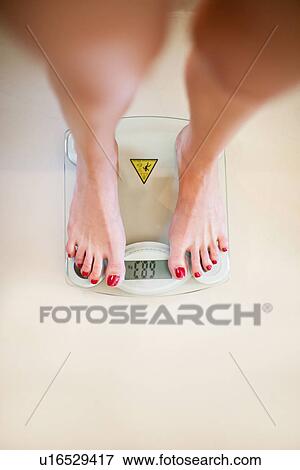 Stock Photo - Woman weighing herself on scale. Fotosearch