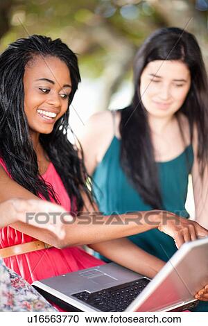 Stock Image - Women using laptop whilst sitting on a tree branch. Fotosearch