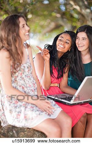 Stock Photo - Women using laptop whilst sitting on a tree branch. Fotosearch