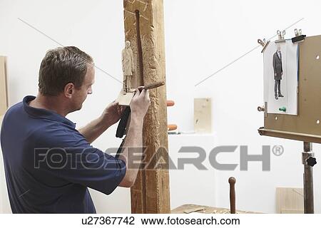 Stock Image - Worker chiseling figure from wood. Fotosearch