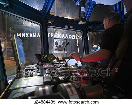 Stock Photography - Worker driving tugboat from wheelhouse. Fotosearch