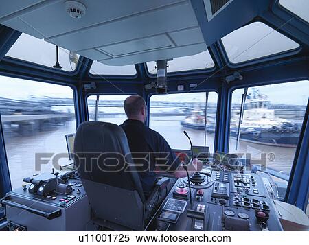 Stock Photography - Worker driving tugboat in wheelhouse. Fotosearch