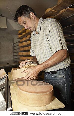 Stock Photo - Worker finishing wheel of cheese in shop. Fotosearch
