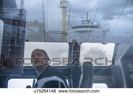Stock Photo - Worker in tugboat wheelhouse at window. Fotosearch