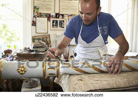 Stock Image - Worker painting carved decorative pole. Fotosearch