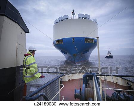 Stock Image - Worker standing on deck of tugboat. Fotosearch