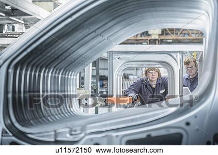 Stock Image - Apprentices inspecting car in factory. Fotosearch