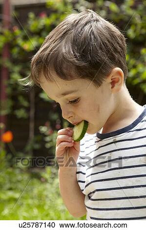 Stock Image - Boy eating cucumber outdoors. Fotosearch