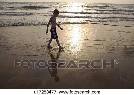 Stock Photo - Boy walking in waves on beach. Fotosearch