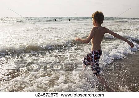 Stock Photo - Boy walking in waves on beach. Fotosearch