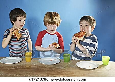 Stock Photograph - Boys eating pizza at table. Fotosearch