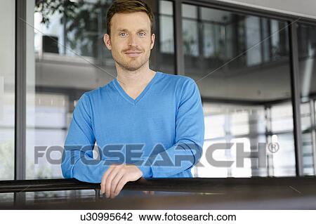 Stock Image - Businessman leaning on railing in office. Fotosearch