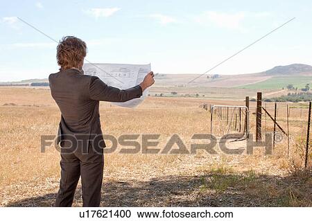 Stock Image - Businessman reading blueprints in field. Fotosearch