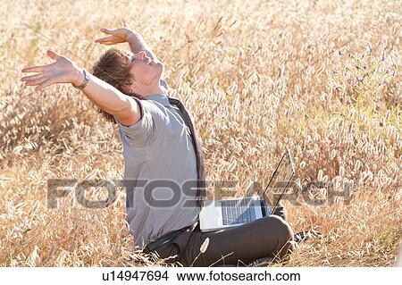 Picture - Businessman using laptop in tall grass. Fotosearch