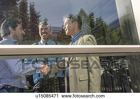 Stock Image - Businessmen shaking hands in office. Fotosearch
