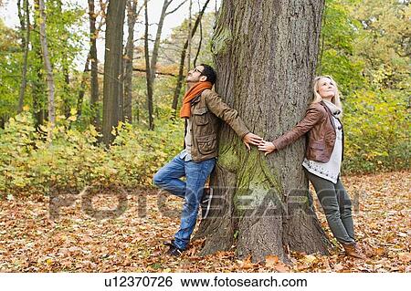 Couple holding hands around tree View Large Photo Image Stock Photograph - Couple holding hands around tree. Fotosearch