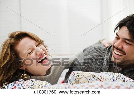 Stock Image - Couple laughing together on bed. Fotosearch