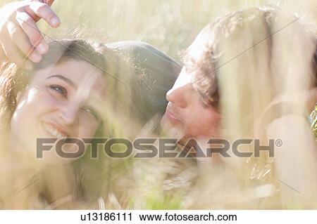 Stock Image - Couple laying together in tall grass. Fotosearch