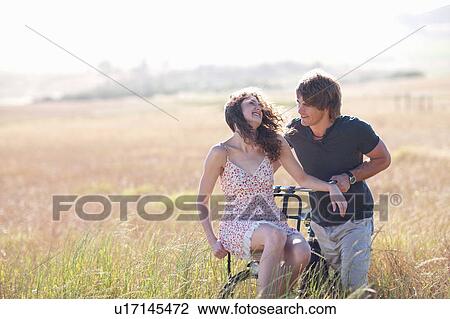 Couple playing on bicycle in tall grass View Large Photo Image Stock Image - Couple playing on bicycle in tall grass. Fotosearch