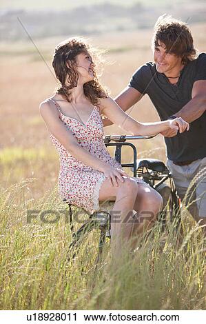 Couple playing on bicycle in tall grass View Large Photo Image Stock Image - Couple playing on bicycle in tall grass. Fotosearch