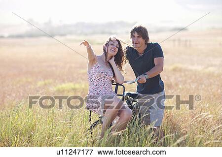 Stock Photo - Couple playing on bicycle in tall grass. Fotosearch