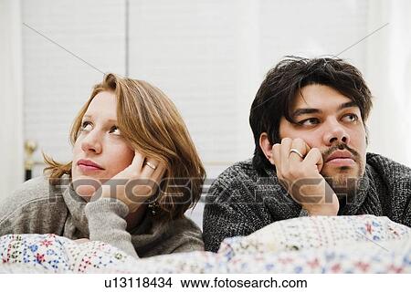 Picture - Couple resting chins in hands on bed. Fotosearch
