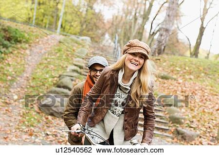 Couple riding bicycle in park View Large Photo Image Stock Image - Couple riding bicycle in park. Fotosearch