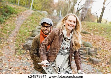 Couple riding bicycle in park View Large Photo Image Stock Image - Couple riding bicycle in park. Fotosearch