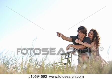 Stock Image - Couple riding bicycle in tall grass. Fotosearch
