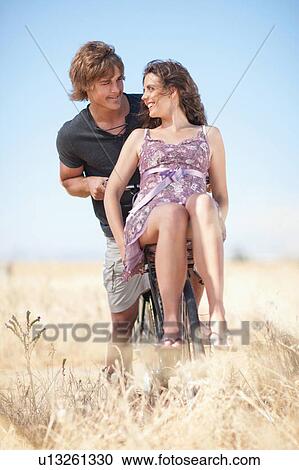 Stock Image - Couple riding bicycle in tall grass. Fotosearch