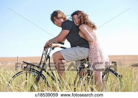 Stock Photo - Couple riding bicycle in tall grass. Fotosearch