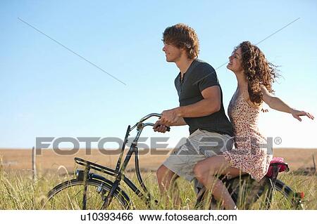 Couple riding bicycle in tall grass View Large Photo Image Stock Photograph - Couple riding bicycle in tall grass. Fotosearch