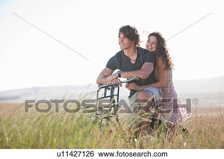 Couple riding bicycle in tall grass View Large Photo Image Stock Photograph - Couple riding bicycle in tall grass. Fotosearch